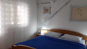 Un dormitorio con cama, mesita de noche, lámpara, ventana con cortina y aire acondicionado instalado en la pared.