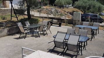 An outdoor seating area with tables and chairs, a stone wall, and a parked car.