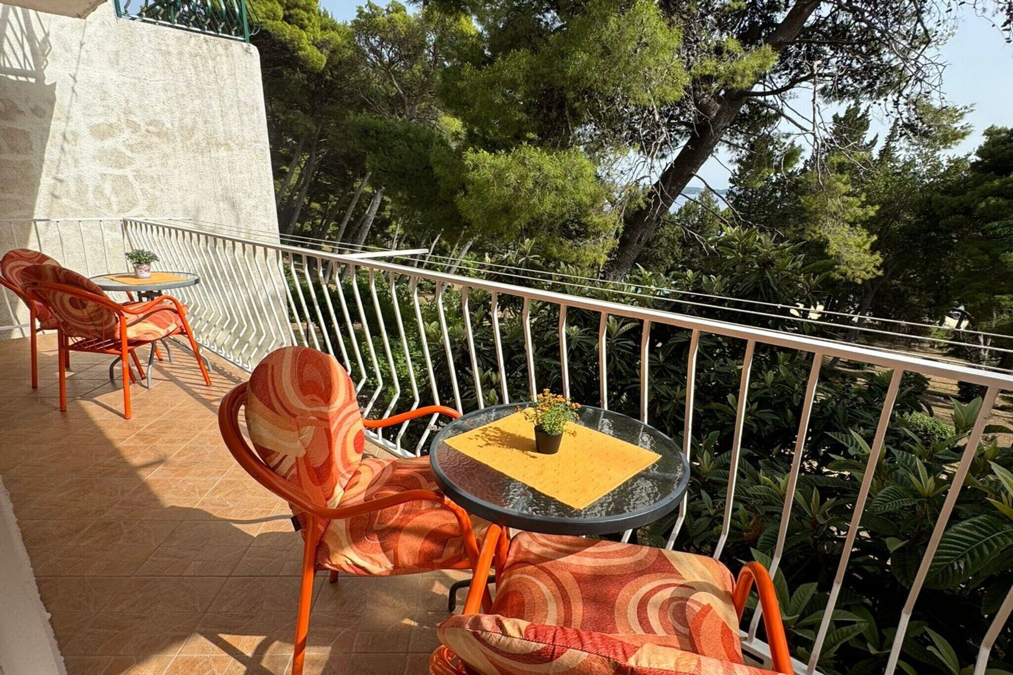 Een balkon met oranje stoelen en een kleine tafel met een plant.