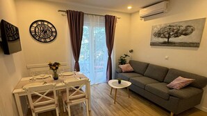 Een moderne woonkamer met een eethoek, een grijze bank en een schilderij van een boom.