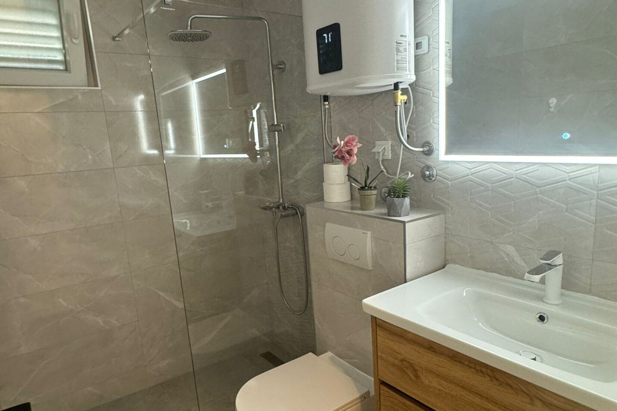 Um banheiro moderno com chuveiro envidraçado, vaso sanitário branco e pia com armário de madeira.