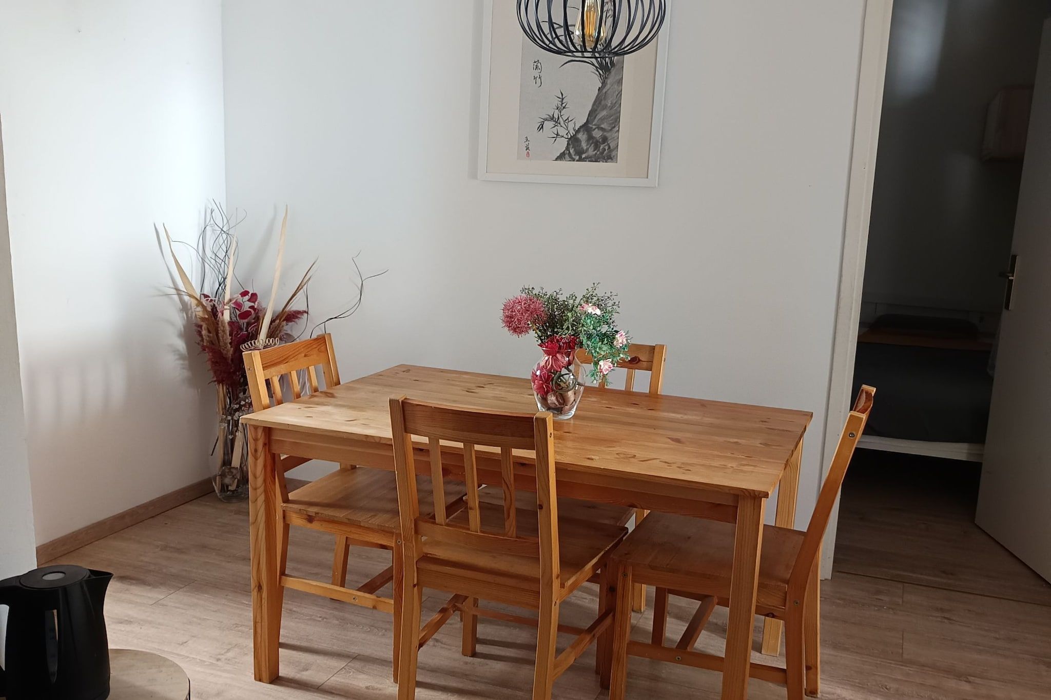 Ein Holztisch mit Stühlen, eine Vase mit Blumen und ein gerahmtes Kunstwerk an der Wand.