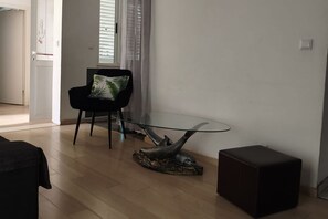 Una sala de estar moderna con una mesa de centro de vidrio, una silla negra con un cojín verde y un reposapiés oscuro.