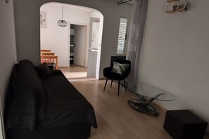 Una sala de estar moderna con un sofá, una mesa de centro de cristal y un sillón. Se ve una puerta que conduce a otra habitación.