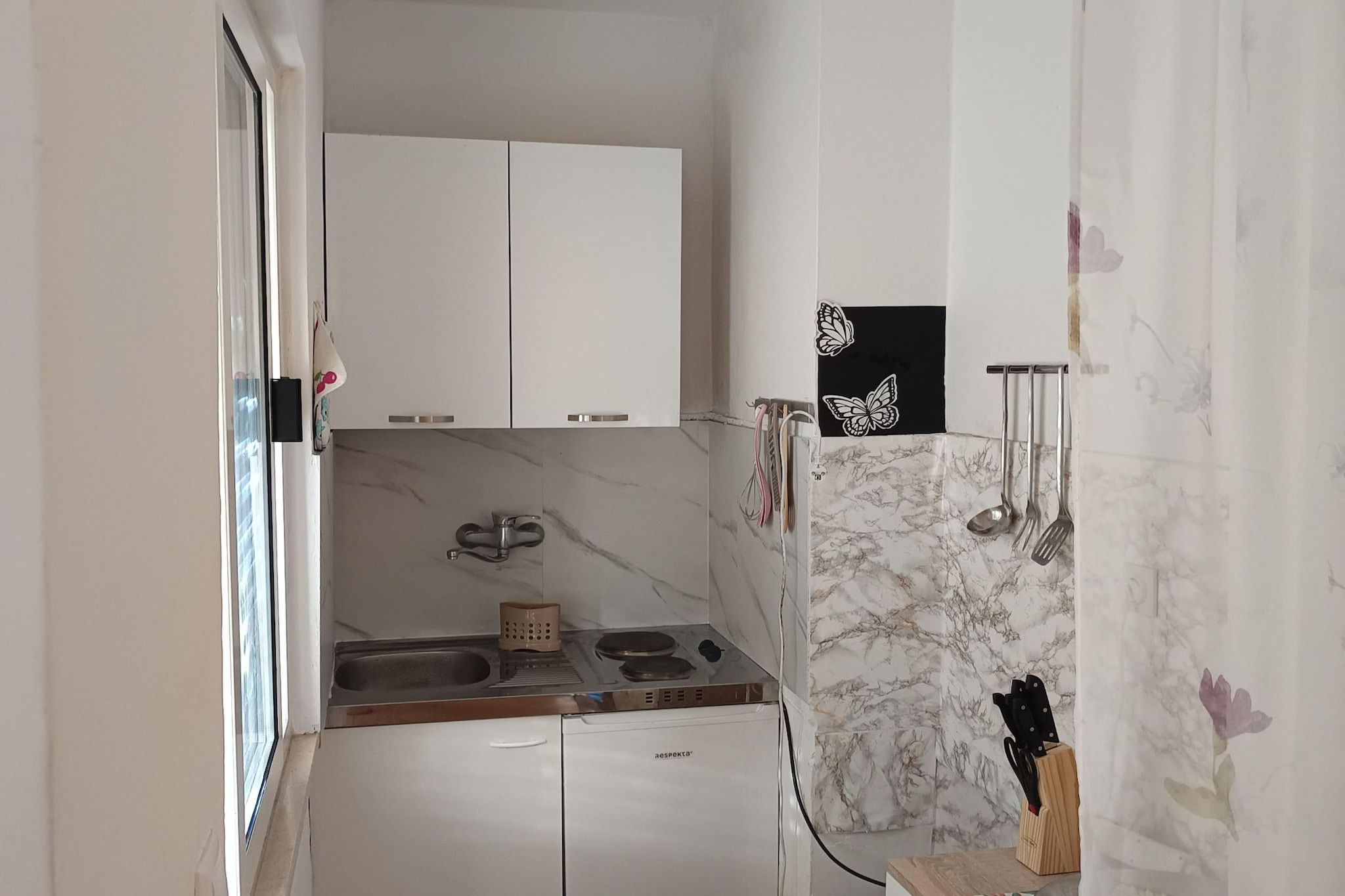 Eine kleine Küche mit weißen Schränken, einer Marmor-Spritzschutzwand und einem Spülbecken.