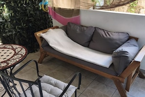 A wooden sofa with cushions, a small round table with a patterned tabletop, and a chair with a cushion.