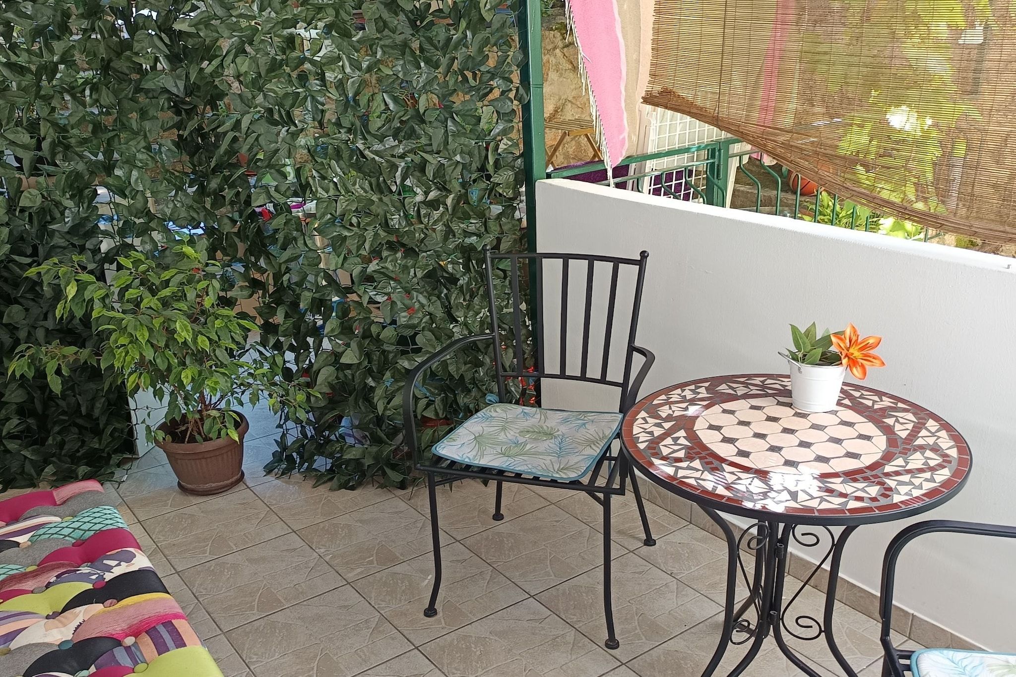 A small outdoor seating area with a chair and a table, surrounded by potted plants and a tiled floor.