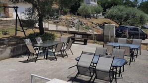 An outdoor seating area with tables and chairs, a stone wall, and a parked car. - Apartments Danijela & Vlado - Two Bedroom Apartment with Balcony and Garden View (Lopar)