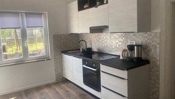 A modern kitchen with a black countertop, white cabinetry, a built-in oven, and a window with a view of the outdoors. - Apartments Danijela & Vlado - Two Bedroom Apartment with Balcony and Garden View (Lopar)