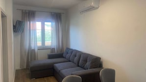 A living room with a sectional sofa, a flat-screen TV mounted on the wall, and a window with curtains. - Apartments Danijela & Vlado - Two Bedroom Apartment with Balcony and Garden View (Lopar)