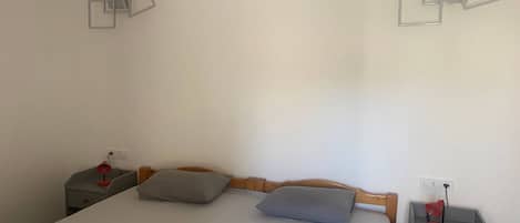 A simple room with a bed, two bedside tables, and a wall-mounted light fixture.