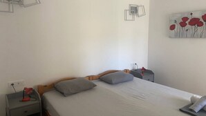 A bedroom with a single bed, two bedside tables, a nightstand, a wall-mounted lamp, and a painting. - Apartments Danijela & Vlado - Two Bedroom Apartment with Balcony and Garden View (Lopar)