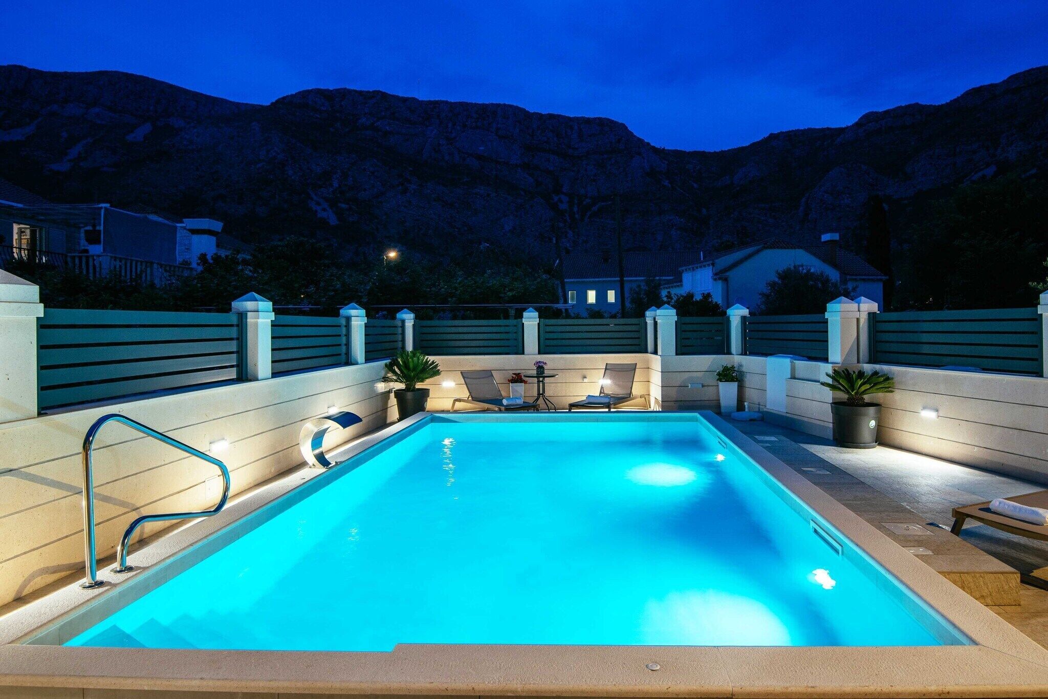Ein rechteckiger Pool mit einer Metallleiter, umgeben von einer niedrigen Mauer und Blumentöpfen.
