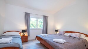 A hotel room with two single beds, a large window with curtains, a wooden floor, and a nightstand with a lamp.