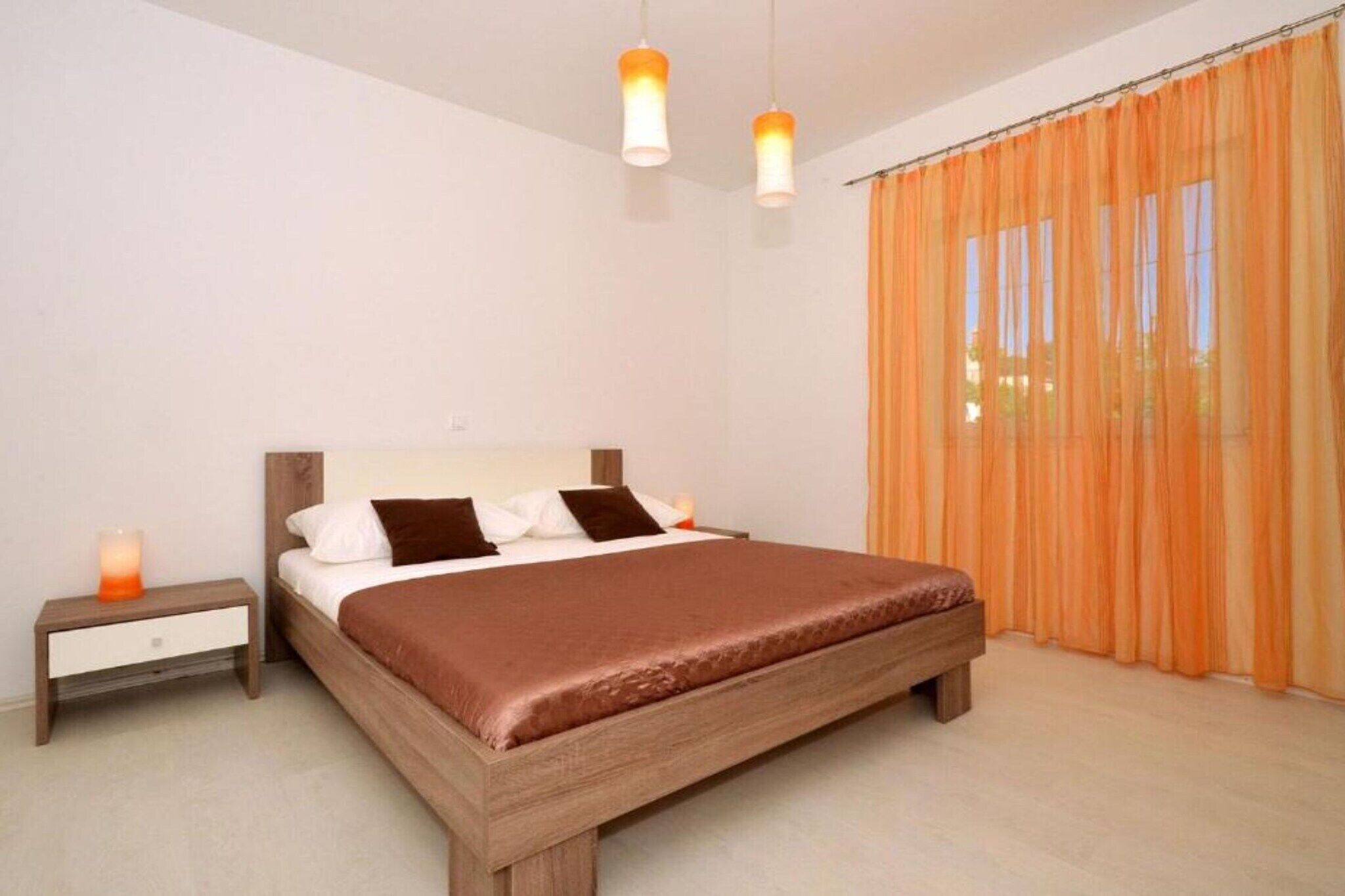 Un dormitorio con cama de madera, dos mesitas de noche y cortinas color naranja.
