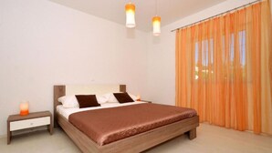Ein Schlafzimmer mit einem hölzernen Bett, zwei Nachttischen, einem Beistelltisch und orangefarbenen Vorhängen.