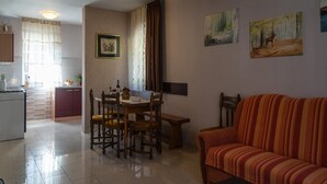 Una sala de estar con un sofá a rayas, una mesa de comedor con sillas y una zona de cocina con refrigerador y armarios.
