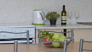 Une cuisine avec une bouilloire blanche, une plante en pot, une bouteille de vin et deux verres posés sur le comptoir.