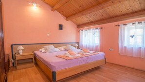 A bedroom with a wooden ceiling, a bed with a purple bedspread, two bedside tables with lamps, and a window with curtains. - Apartments Bonic - Two Bedroom Apartment (Veli Losinj)