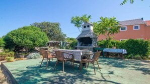 An outdoor patio with a table and chairs, a stone structure, and a red building in the background. - Apartments Bonic - Two Bedroom Apartment (Veli Losinj)
