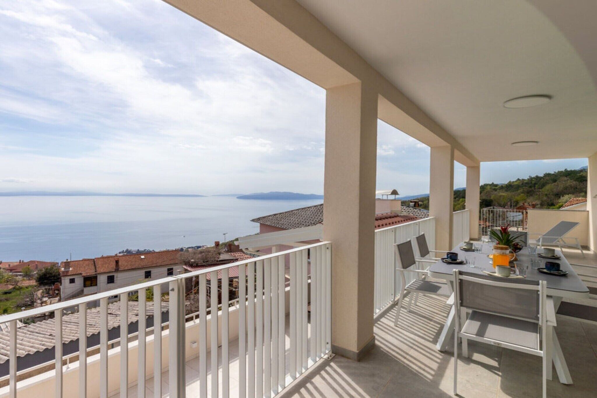 A balcony with a table set for two, overlooking a coastal view.