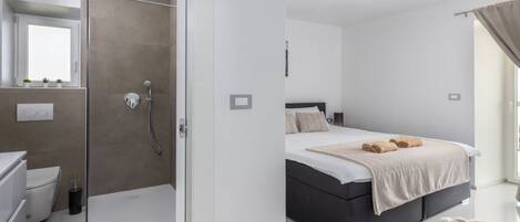 A modern bedroom with a large bed, a bedside table, and a shower area.