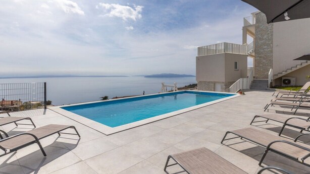 A swimming pool with a view of the sea, surrounded by lounge chairs and a building with a stone facade. - Apartments Bregha - Three Bedroom Apartment with Terrace (Matulji)