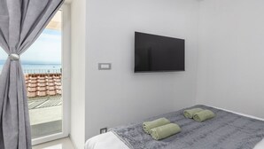 Een slaapkamer met een bed, een flatscreen-tv en uitzicht op de zee door een raam met gordijnen.