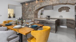 Een moderne keuken met een boog van natuursteen, een houten eettafel en gele stoelen.