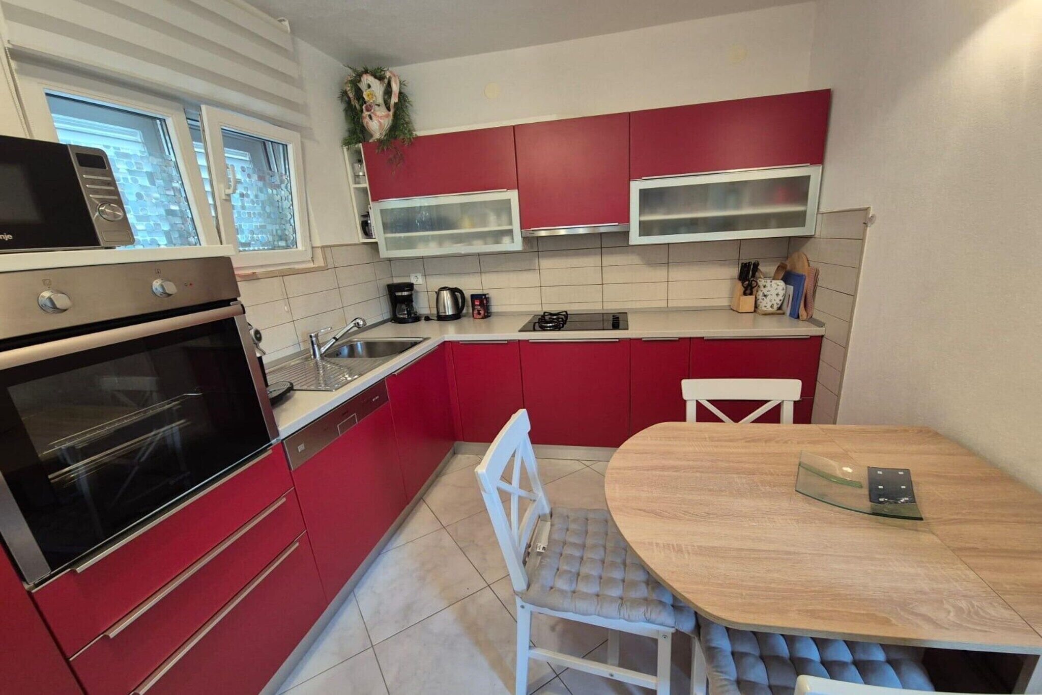Une cuisine avec des meubles de rangement rouges, un four en acier inoxydable, un évier et une table à manger avec des chaises.