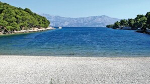 Une plage de galets qui mène à une mer calme, avec des montagnes en arrière-plan.