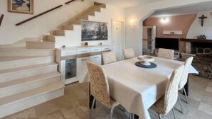 Un coin repas avec une table dressée pour quatre personnes, une cuisine dotée de meubles blancs et un escalier menant à un autre niveau.
