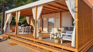 A wooden deck with a covered seating area, a pool, and a building with a sign that reads "ADRIA". - Two Bedroom Mobile Home (Orebic)