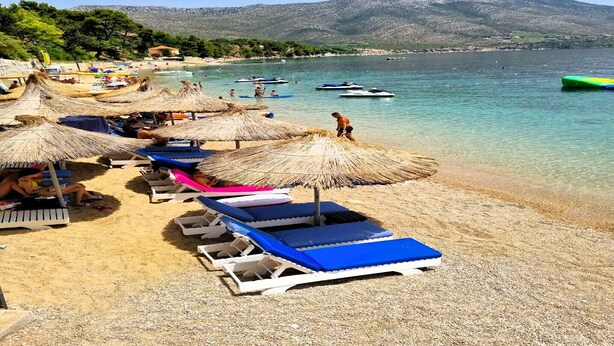 A beach with sun loungers and thatched umbrellas, a clear view of the sea, and boats in the background. - Two Bedroom Mobile Home (Orebic)