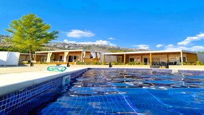A swimming pool with a tiled edge, a covered seating area, and a mountain backdrop. - Two Bedroom Mobile Home (Orebic)
