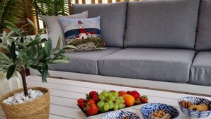A grey sofa with a cushion featuring a lighthouse, a potted plant, and bowls of fruits and nuts on a white table. - Two Bedroom Mobile Home (Orebic)