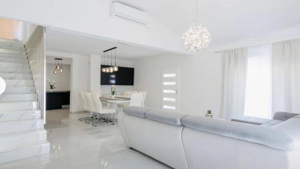 Un salon moderne avec un canapé blanc, un coin repas comprenant une table et des chaises, et un escalier menant à un autre niveau.