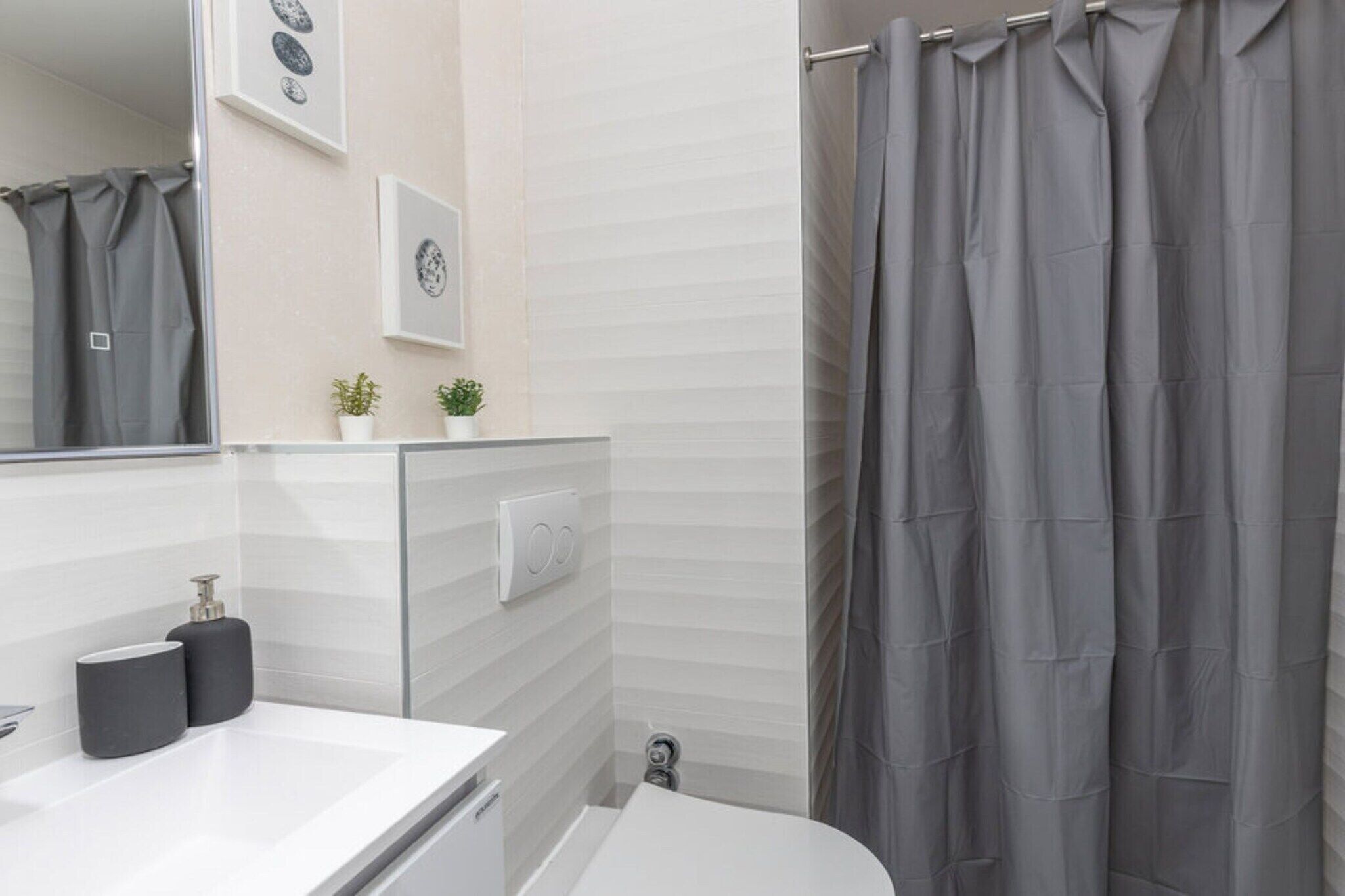 Een moderne badkamer met een witte wasbak, twee zwarte zeepdispensers, een wit toilet en een grijze douchegordijn.