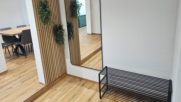 A modern interior with a wooden floor, a mirrored wall, and a black metal rack.