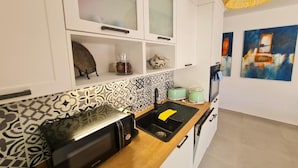 Una cocina moderna con armarios blancos, un salpicadero estampado, un tostador, un lavamanos y una lámpara colgante.