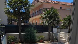 Un edificio residencial con balcón, palmeras y entrada protegida por un portón.