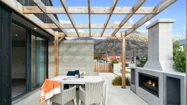 Une terrasse extérieure avec une table et des chaises, une structure en forme de pergola et une cheminée intégrée.