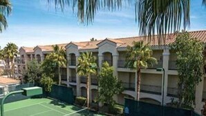 Una cancha de tenis rodeada por un edificio con varios balcones y palmeras.