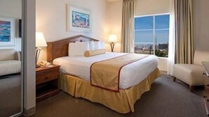 Una habitación de hotel con una cama, una mesita de noche, una silla, una ventana con vistas y un cuadro en la pared.