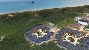 An aerial view of a coastal residential area with modern houses, a beach, and a ferry in the distance.