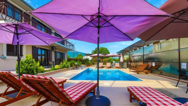 A pool area with sun loungers and umbrellas, surrounded by buildings.