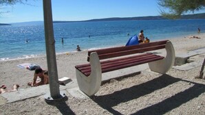 A beach with a wooden bench, people sunbathing, and a calm sea.