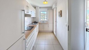 A narrow kitchen with white cabinets, a stove, and a window. - apartment near the beach (Fréjus)