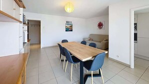 A modern kitchen with a wooden table and chairs, a white countertop, and a hanging light fixture. - apartment near the beach (Fréjus)