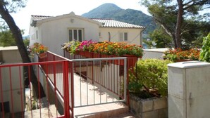 A residential building with a white facade, a red gate, and a mountain in the background. - Guest House Sobra 38 - Studio with Balcony and Sea View (Sobra)